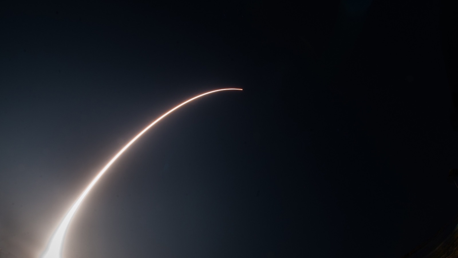 A long-exposure arc of a satellite launch across a night sky